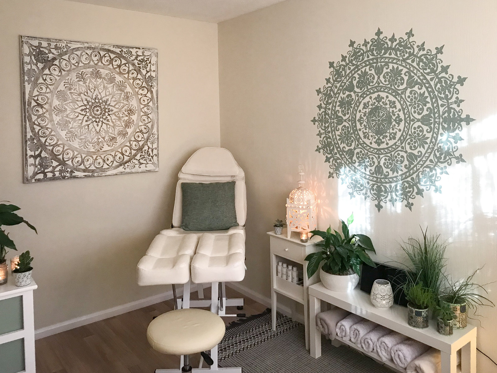 Claire's treatment room in Crowborough: a cream recliner chair with a sage cushion, two large carved mandala panels on the wall, plants, candles and rolled towels